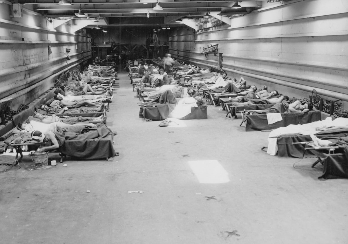 09-7930-2 Once it discharged its wheeled cargo of DUKWs, jeeps and trucks on the invasion beach, an LST tank deck offered ample space for casualties. In the early days of the Pacific campaign there were very few hospital ships in theater, and landing craft and troop transports with negligible medical services offered the only available transportation for the wounded. Original title: First aid to casualties in LST. BuAer 43557; Herman, Battle Station Sick Bay, Naval Institute Press, Photo 13 related to Transformative Furniture: Chairs That Become Beds