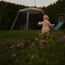 A baby in a floral romper walking across a grassy backyard at golden hour related to The Regalo My Cot Portable Toddler Bed: Comfort and Convenience on the Go