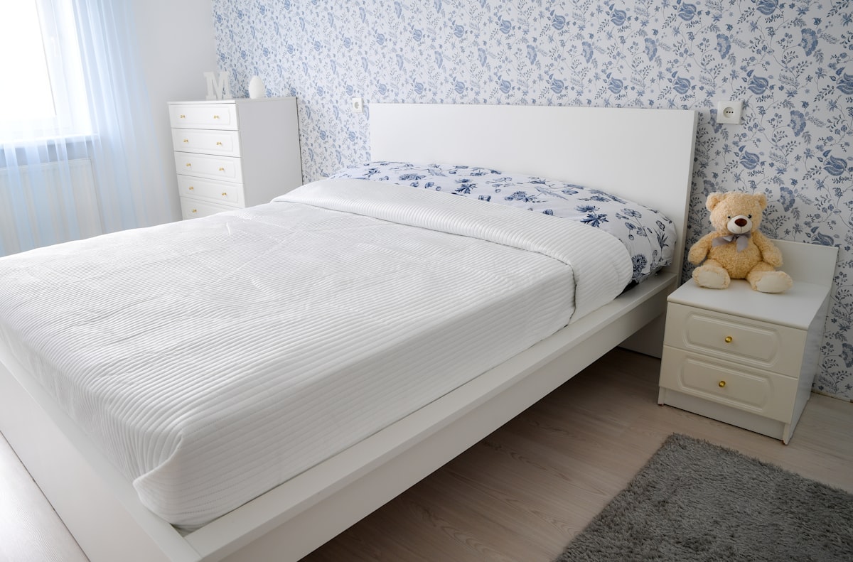 A bright and cozy modern bedroom interior featuring a white double bed, a matching nightstand with a teddy bear, and elegant blue and white floral wallpaper.📸 Photo by me IG: @margoevardson related to Elevate Your Bedroom with a Stylish White Platform Bed