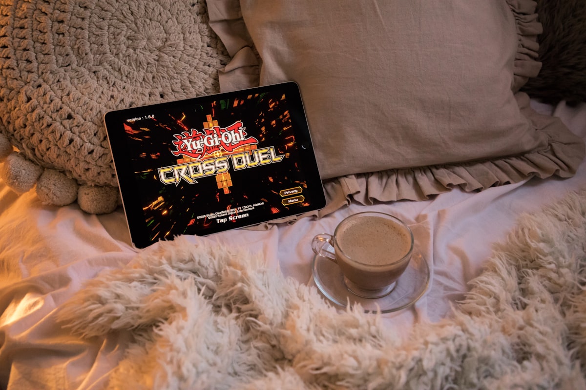 A cozy bed featuring a tablet (iPad) playing "Yu-Gi-Oh! Cross Duel" on display + a cup of cappuccino || I decided to join in Konami's (Yu-Gi-Oh! Card Game 25th Anniversary) fun & create a series of photos featuring the latest Yu-Gi-Oh games/apps || 📸 Photo by: Jovan Vasiljević related to Revolutionizing Your Slumber: The Ultimate Chili Pad for Bed Experience