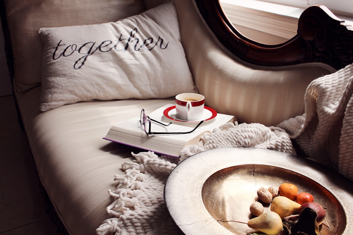 A cozy sofa with a pillow, book, teacup, and fruit. related to The Versatility of a Day Bed: Transforming Your Space