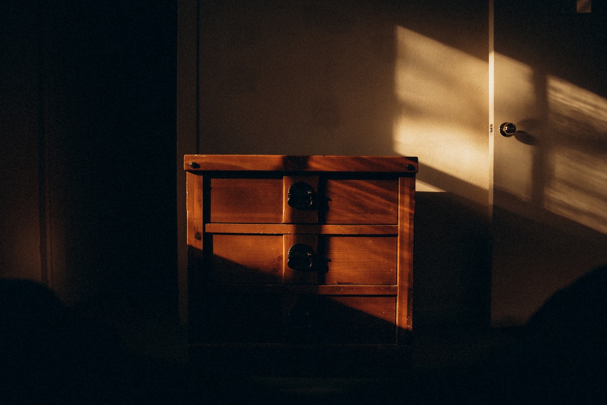 A dark room with a small chest of drawers related to The Evolution of End of Bed Dressers: A Look Back and a New Era