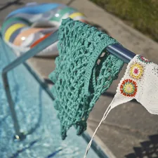 a green crocheted towel hanging on a rail next to a swimming pool related to Crochet Window Valance