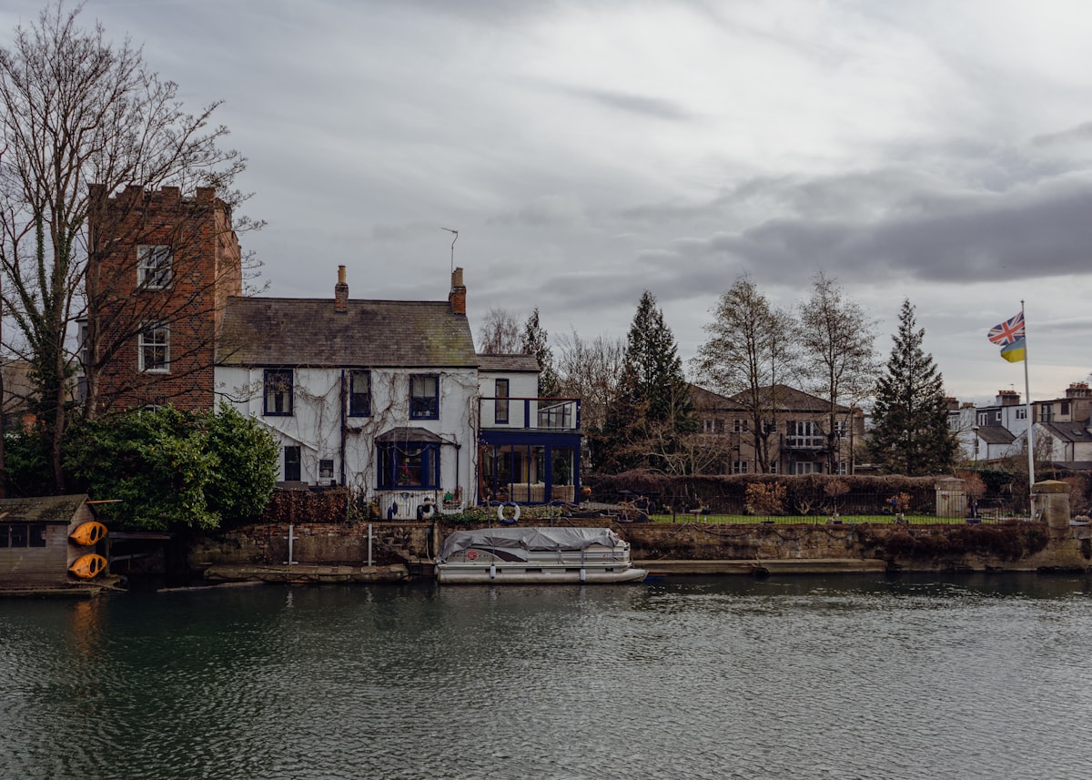 a house sitting on the side of a river next to a boat related to Escape to Tranquility: A Riverside Bed and Breakfast Experience