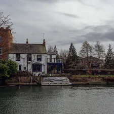 a house sitting on the side of a river next to a boat related to Escape to Tranquility: A Riverside Bed and Breakfast Experience