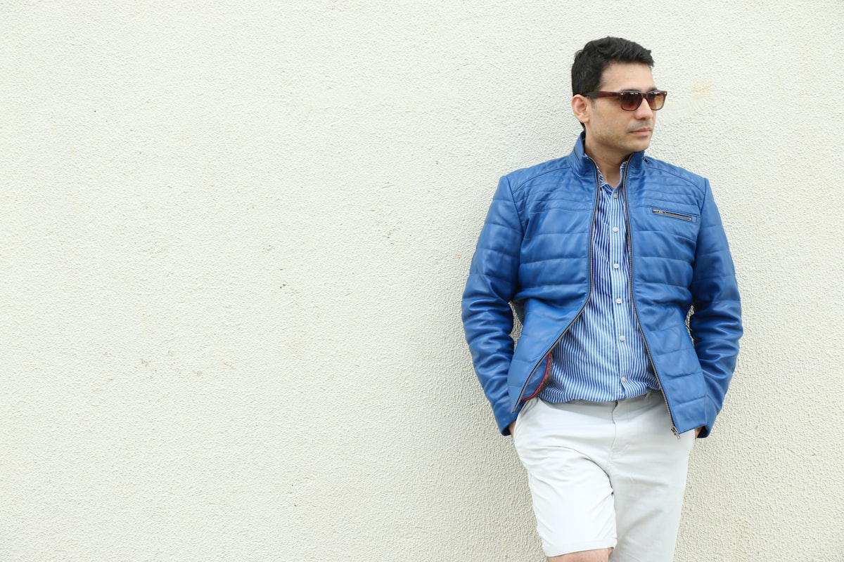 a man in a blue jacket leaning against a white wall related to Experience Luxury with our Quilted Coverlet Hotel Collection