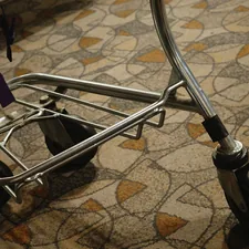 A metal luggage cart sits on patterned carpet. related to Elevate Your Space with Bed Risers for Wheels: A Game-Changer for Your Home