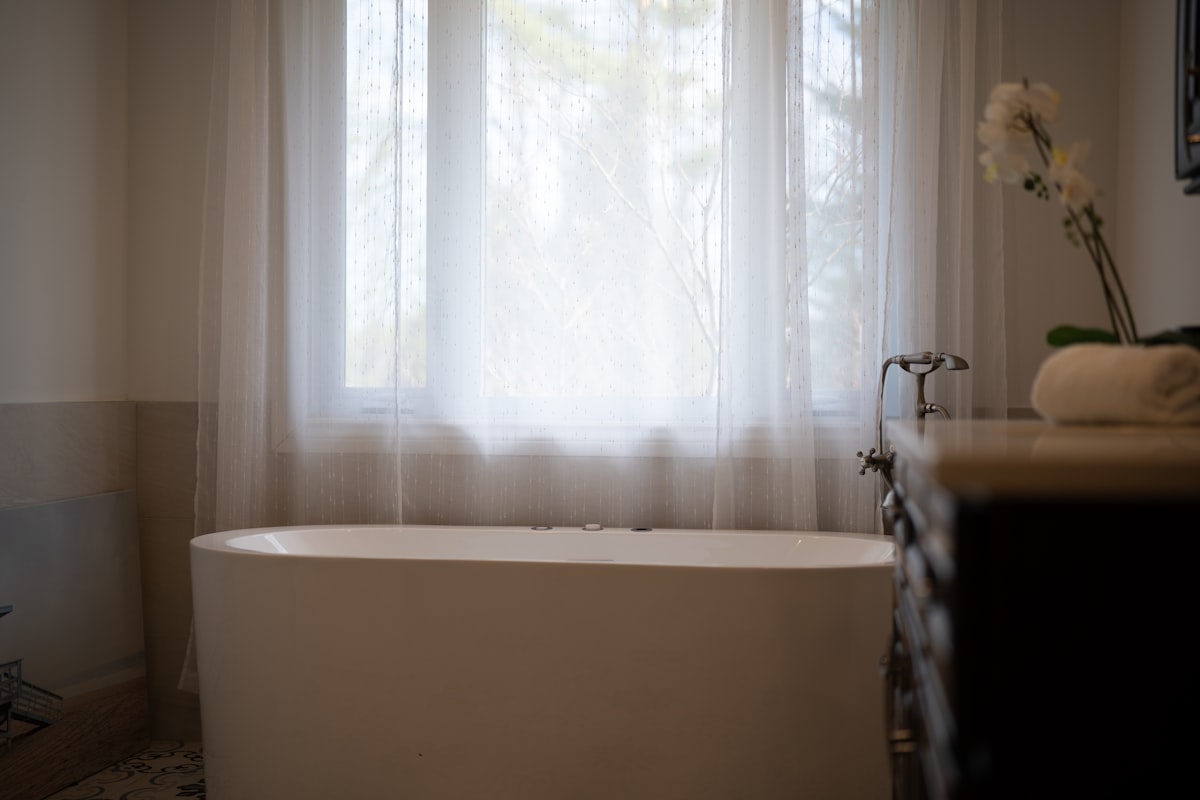 A modern bathtub with sheer curtains and a flower. related to Bathroom Curtain Valance