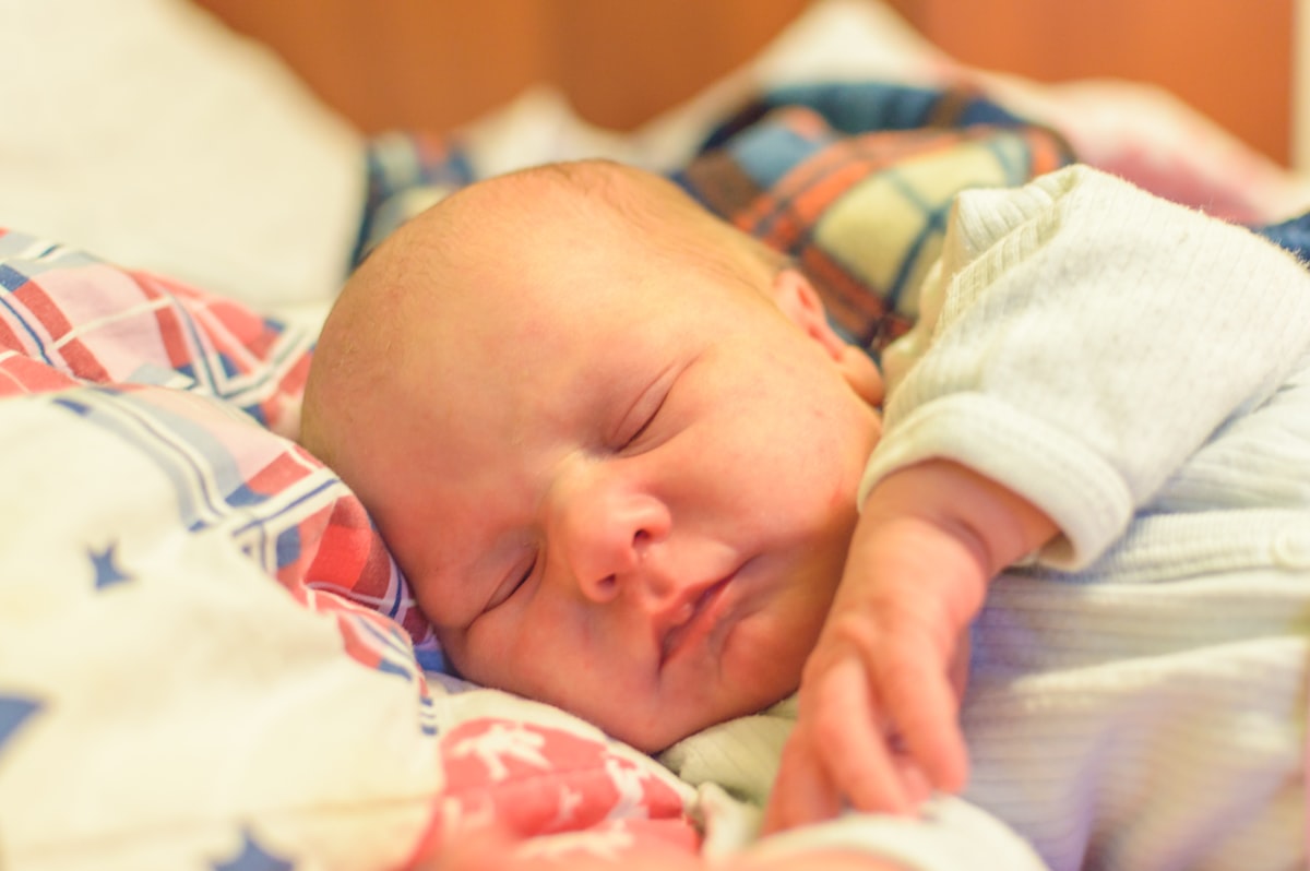 a newborn baby sleeping sweetly in a blanket related to Sleeping with Baby in Bed: Exploring the Pros and Cons