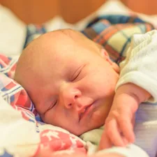 a newborn baby sleeping sweetly in a blanket related to Sleeping with Baby in Bed: Exploring the Pros and Cons