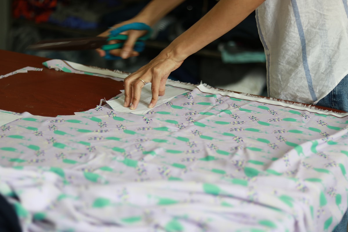 a person cutting a piece of fabric with a pair of scissors related to Creating a Pattern for Scalloped Valance