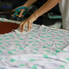a person cutting a piece of fabric with a pair of scissors related to Creating a Pattern for Scalloped Valance