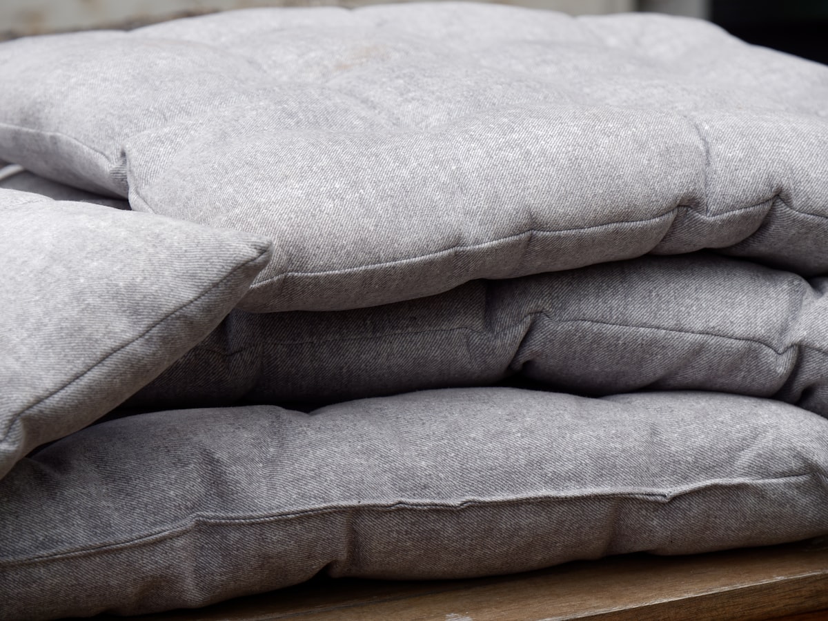 a pile of pillows sitting on top of a wooden table related to Linen Quilts & Coverlets: Timeless Elegance for Your Bed