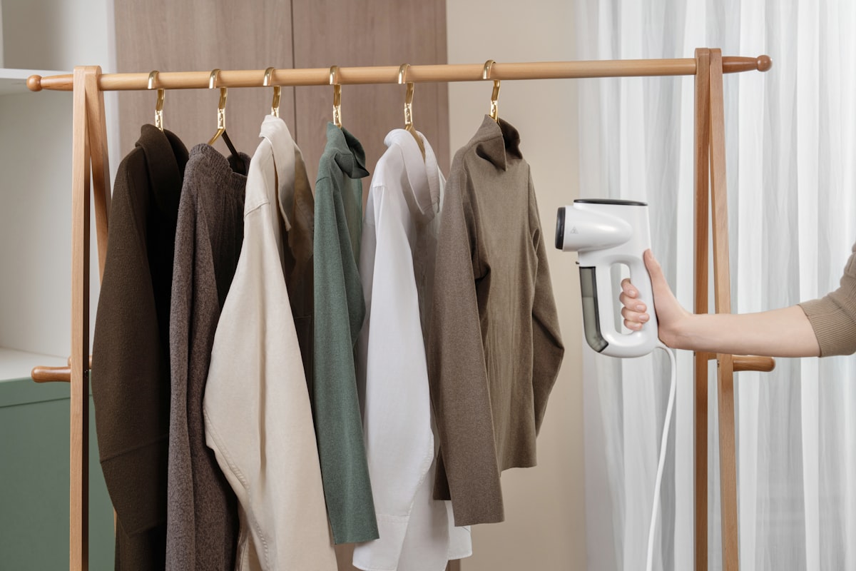 A row of clothes hanging on a wooden rack being effortlessly steamed with a compact vacuum steamer related to Revitalize Your Wardrobe: The Ultimate Guide to Clothes Steamers from Bed Bath & Beyond