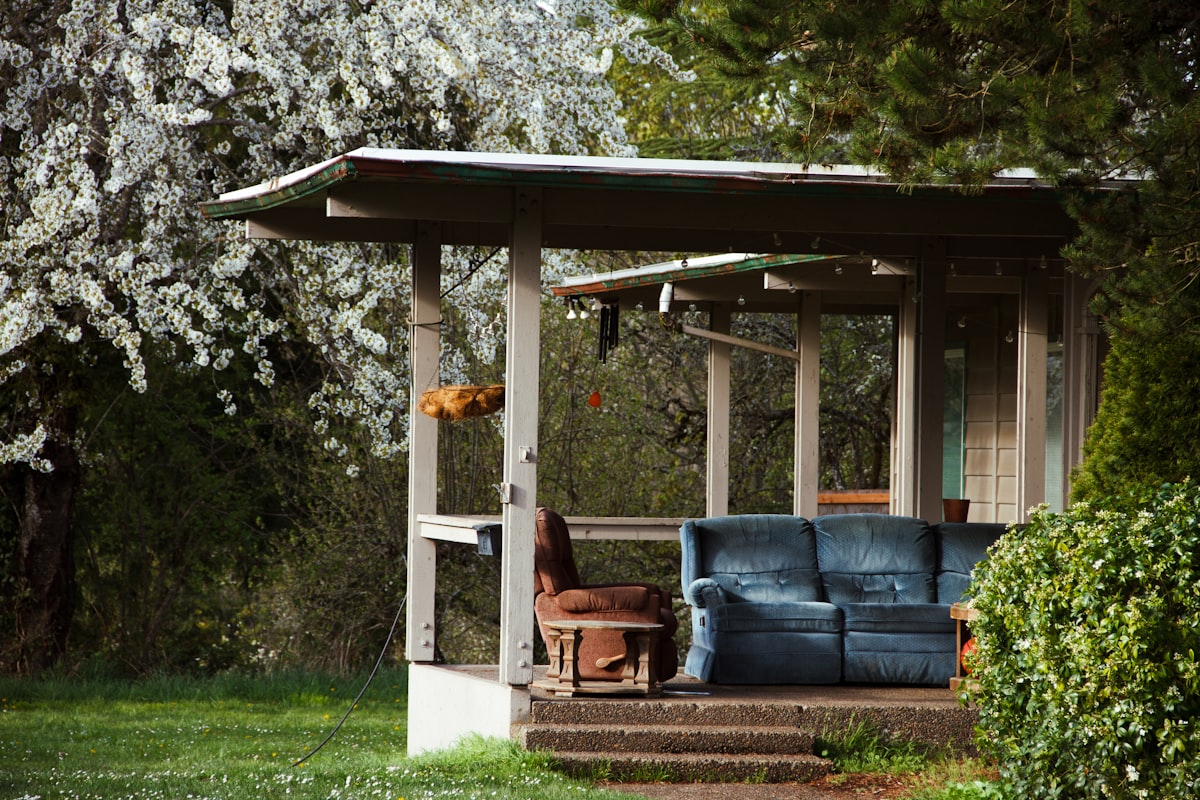 A rustic porch with a couch and chair. related to Warm Up Your Outdoor Space with a Chiminea: Where to Find the Perfect One