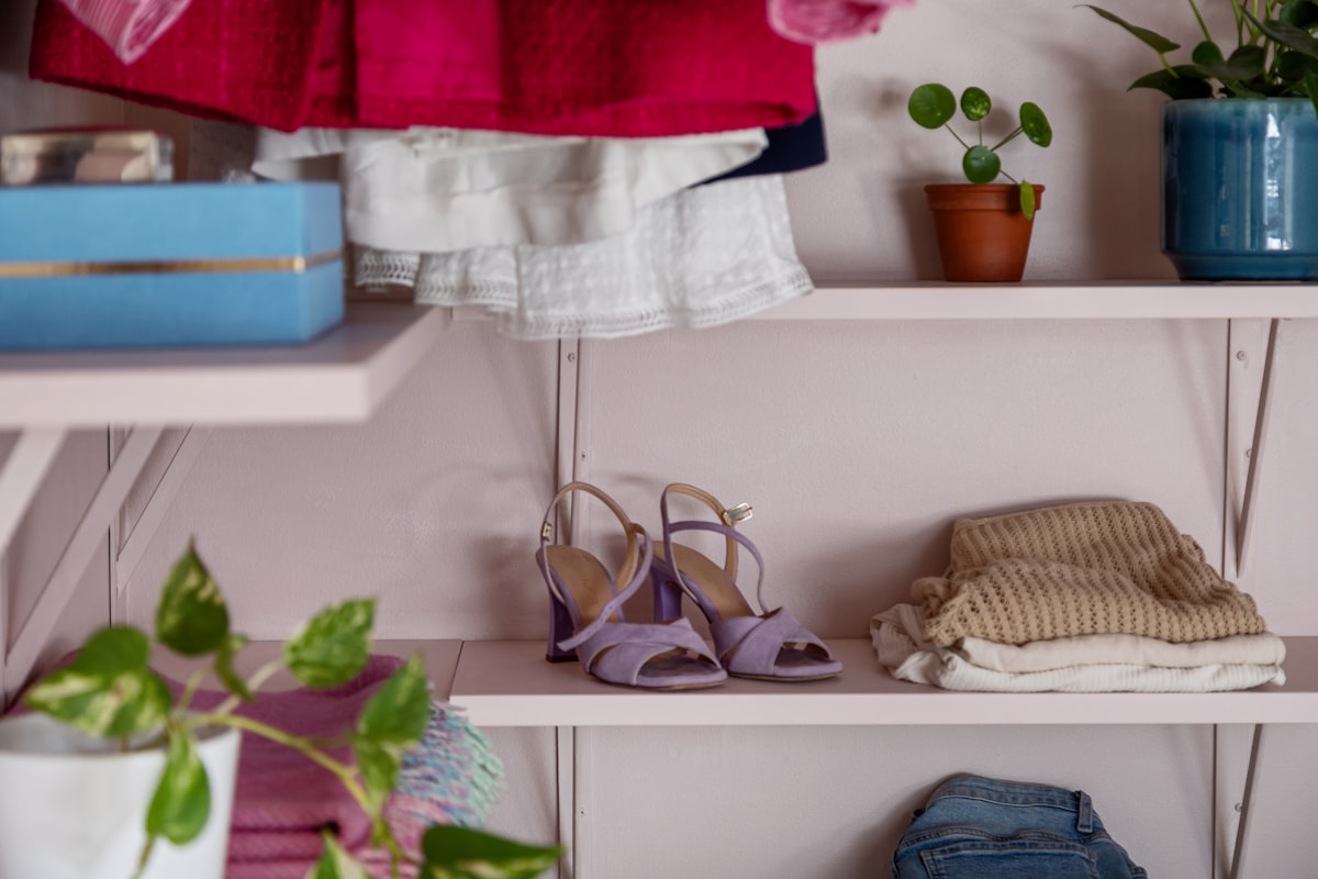 A shelf filled with clothes and shoes next to a potted plant related to Taming the Entryway Chaos: Creative Shoe Storage Solutions