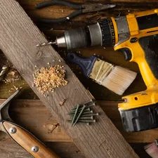 A variety of tools, including a hammer and cordless drill, sit on top of a table made of wood boards.  related to Step-by-Step Guide to Crafting a Wooden Bed Frame