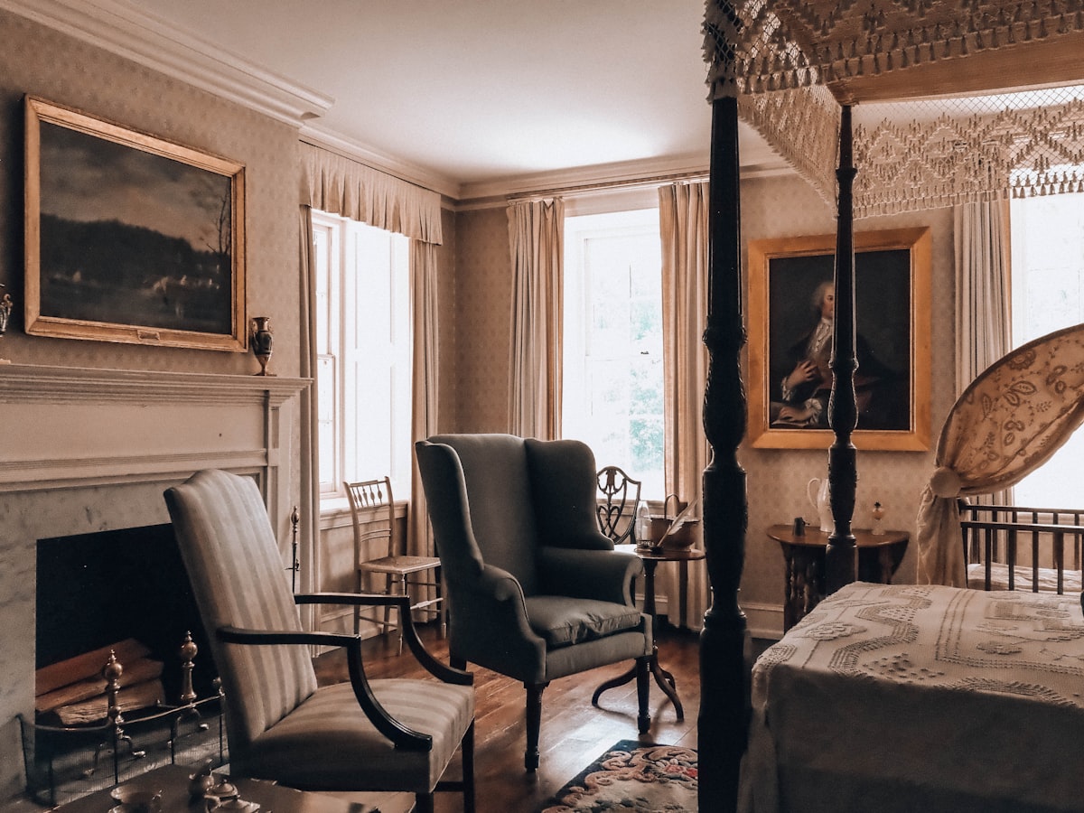 A vintage bedroom with a four-poster bed, fireplace, and armchairs. related to Ultimate Guide to Four Post Beds: Style and Comfort