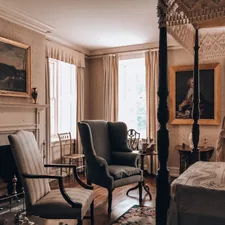 A vintage bedroom with a four-poster bed, fireplace, and armchairs. related to Ultimate Guide to Four Post Beds: Style and Comfort