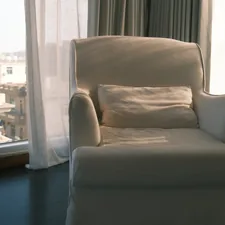 A white armchair with a pillow by the window. related to The Ultimate Space-Saving Solution: Chairs That Convert to Beds