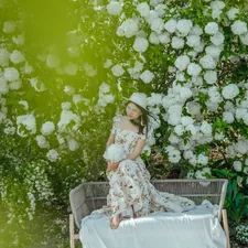 A woman in a dress poses among blossoms. related to Blossoming Style: The Ultimate Guide to Floral Crib Bedding