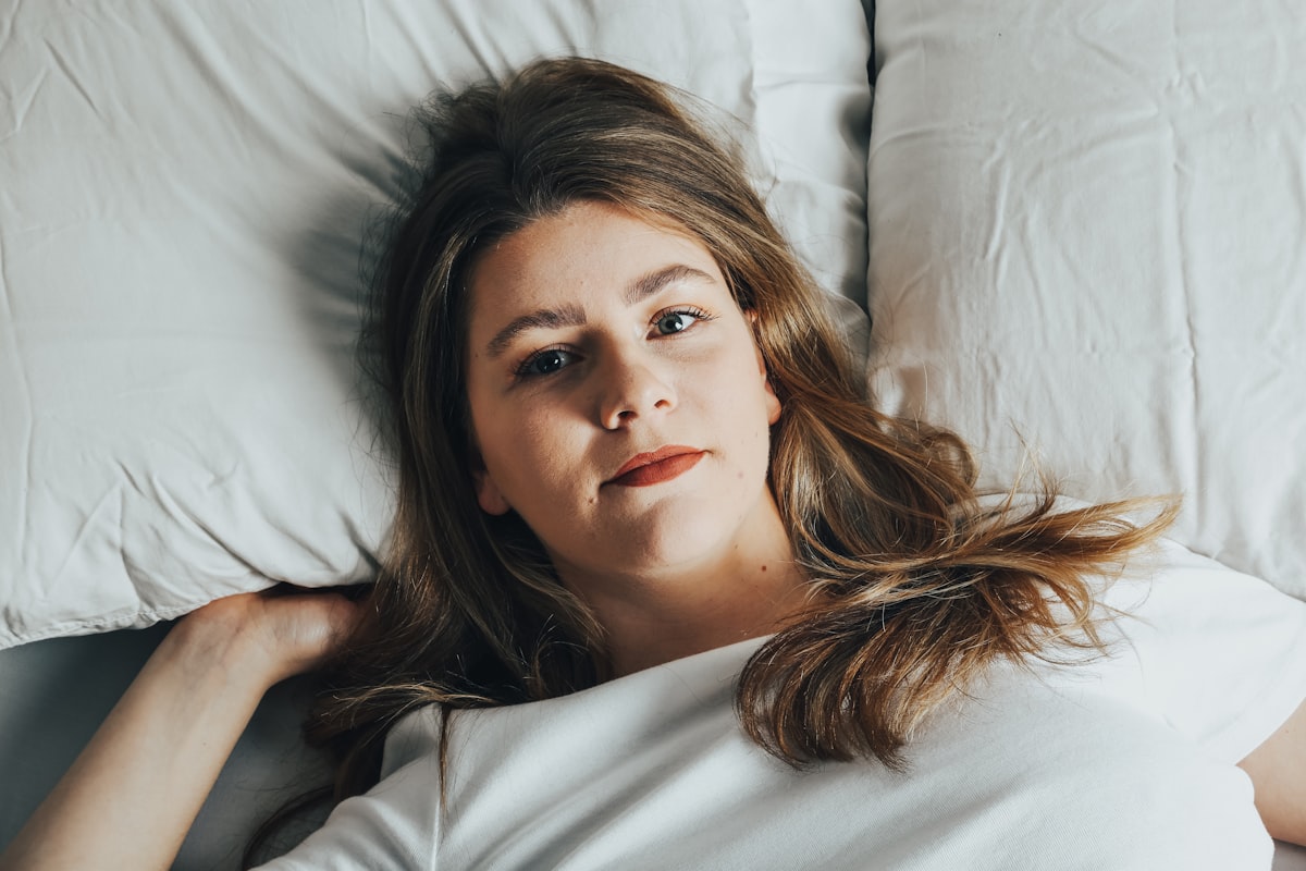 a woman laying on a bed with white sheets related to The Unwelcome Hitchhiker: Dealing with Bed Bugs in Hair