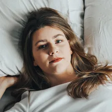 a woman laying on a bed with white sheets related to The Unwelcome Hitchhiker: Dealing with Bed Bugs in Hair