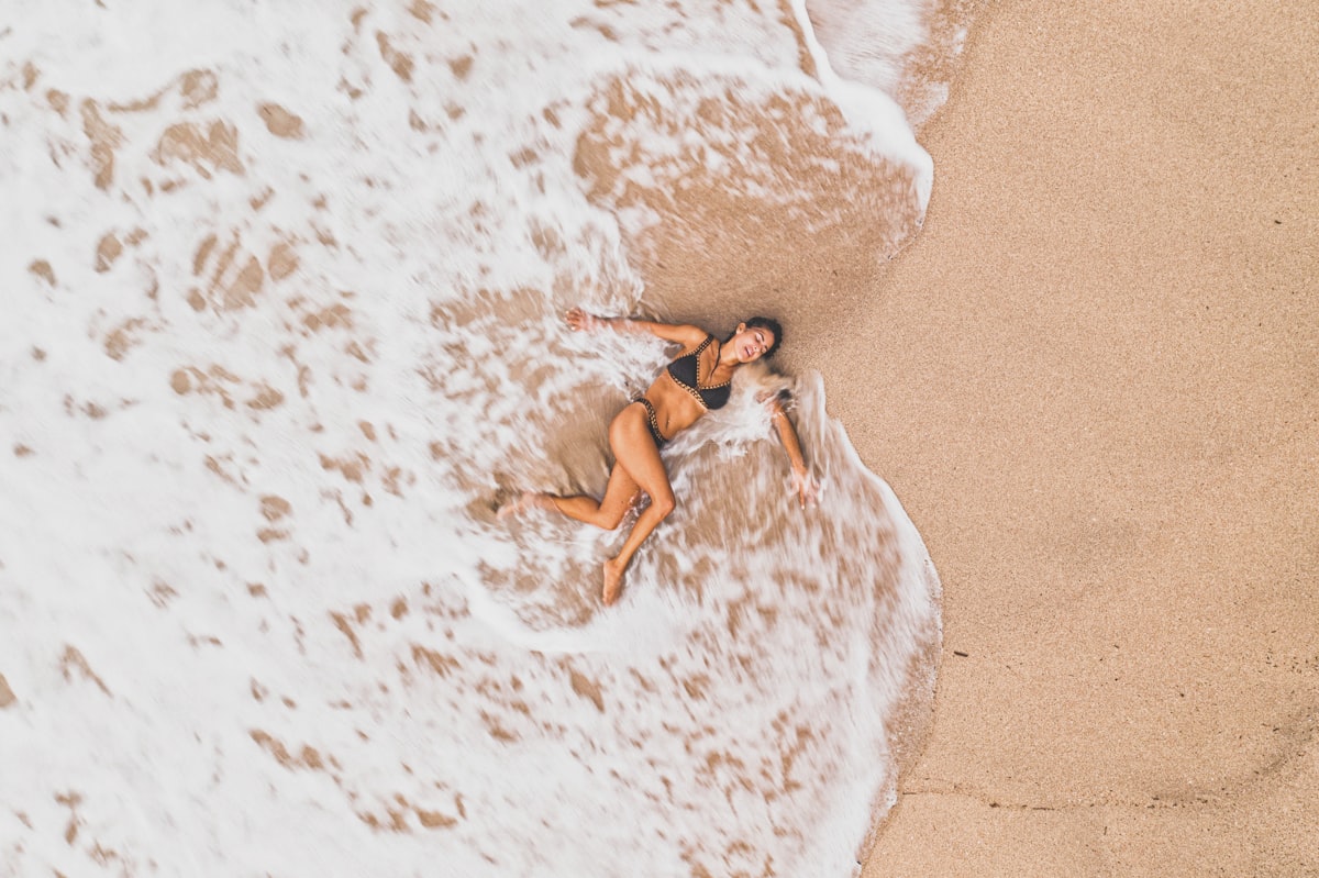 a woman laying on top of a sandy beach next to the ocean related to The Ultimate Guide to Tanning Bed Lotions at Walmart