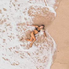 a woman laying on top of a sandy beach next to the ocean related to The Ultimate Guide to Tanning Bed Lotions at Walmart
