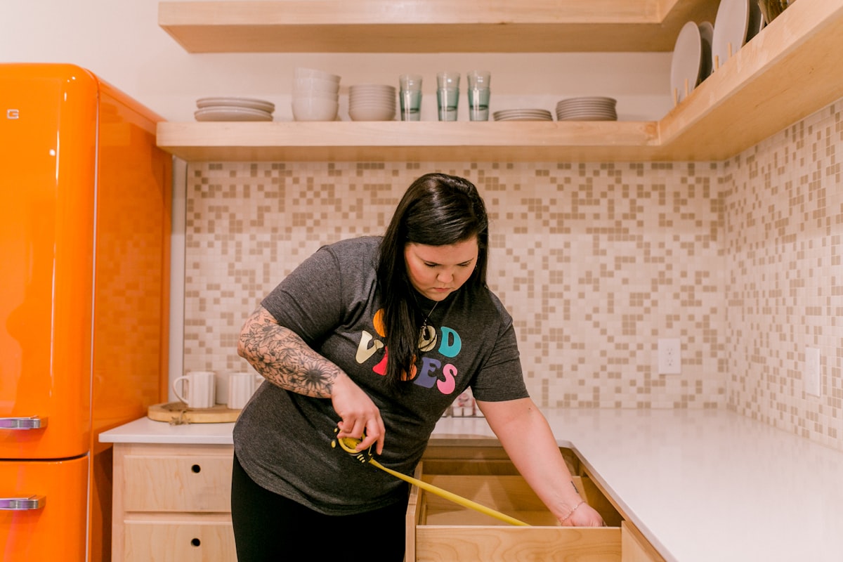 A woman measures a kitchen drawer with a tape measure. related to Maximize Your Space with a Full-Size Storage Bed