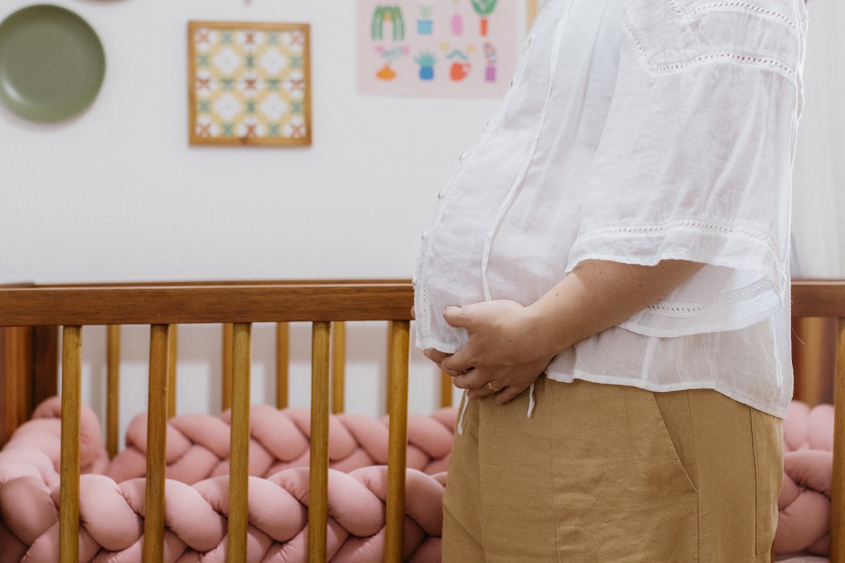 A woman standing in front of a baby crib related to Dreamy Slumber: How to Create a Luxurious Pink and Gold Crib Bedding Set