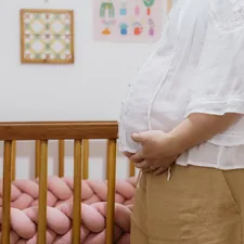 A woman standing in front of a baby crib related to Dreamy Slumber: How to Create a Luxurious Pink and Gold Crib Bedding Set