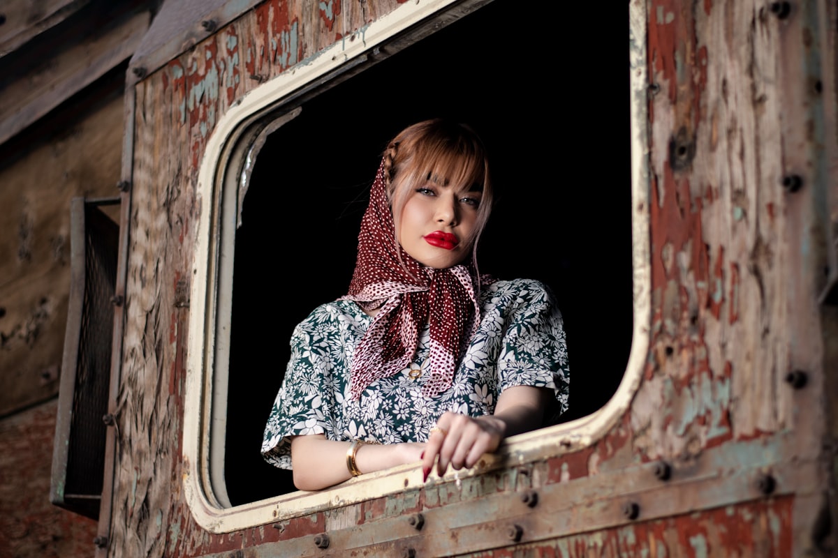 a woman with a scarf on looking out of a window related to Scarf Valance: Creative Window Treatment Ideas