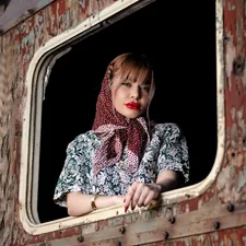 a woman with a scarf on looking out of a window related to Scarf Valance: Creative Window Treatment Ideas