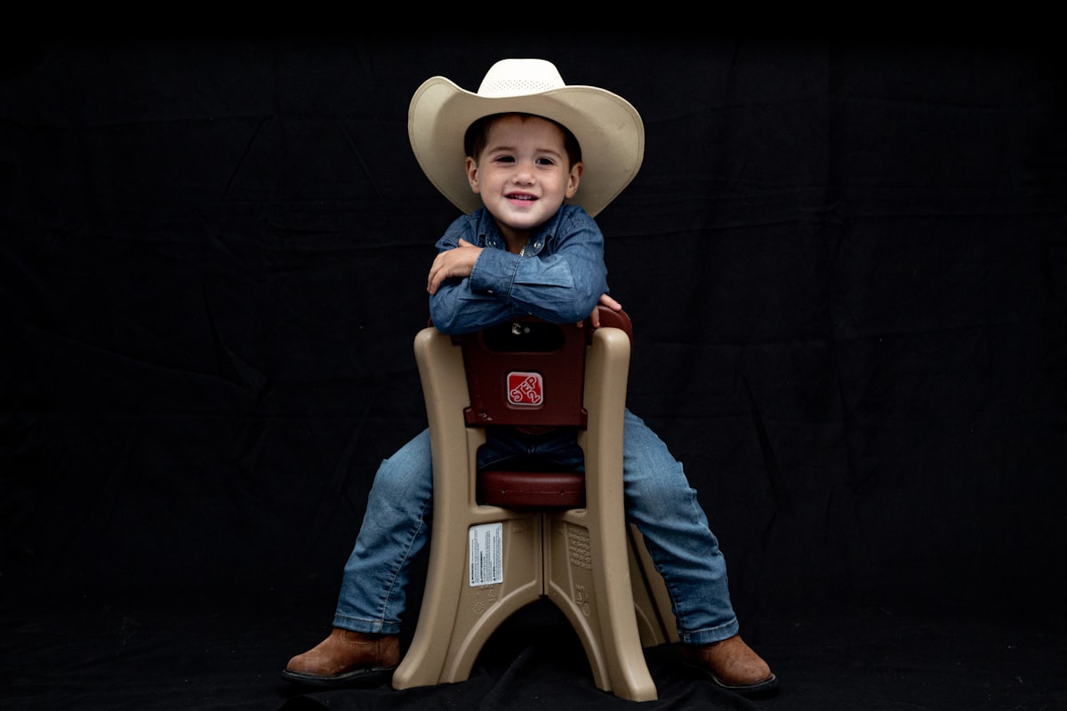 a young boy wearing a cowboy hat sitting on a chair related to Western Baby Bedding Essentials