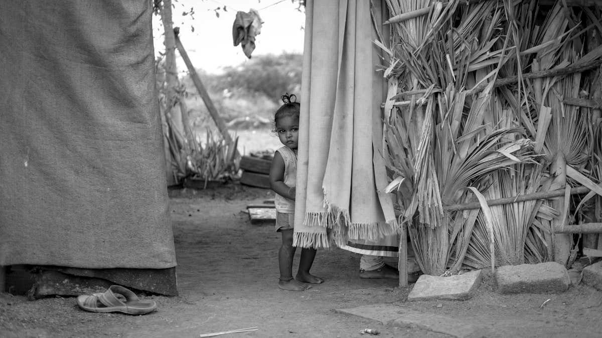 a young girl standing next to a tall grass hut related to How to Access Free Beds for Low-Income Families: Resources and Tips