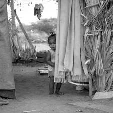 a young girl standing next to a tall grass hut related to How to Access Free Beds for Low-Income Families: Resources and Tips