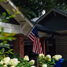 American flag hanging on a house porch with white flowers. related to Charming Escapes: Your Guide to Atlanta's Best Bed and Breakfasts