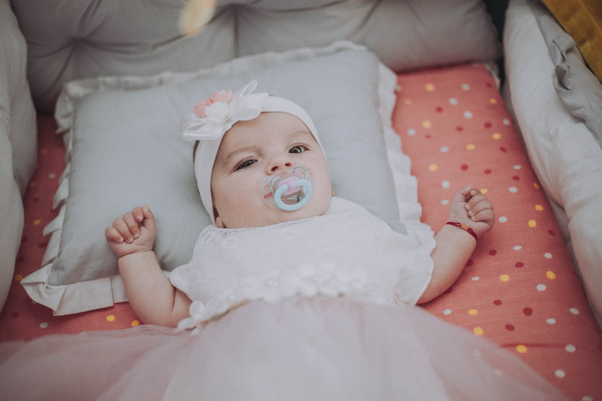 baby in white dress lying on bed related to Cozying Up Your Baby Girl: Trends and Essentials for Baby Girl Crib Bedding