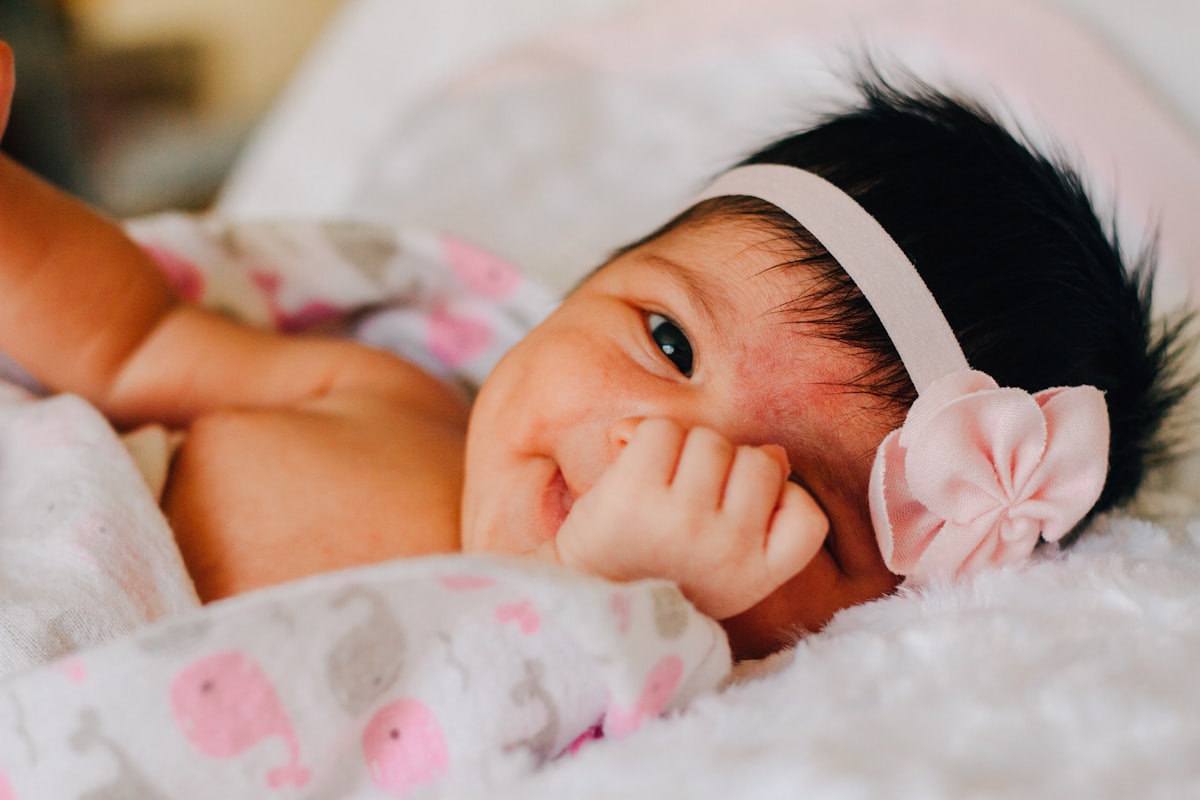 baby wearing white floral headband lying on bed while smiling related to Sweet Dreams in the Dark: A Guide to Black and Pink Crib Bedding