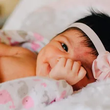 baby wearing white floral headband lying on bed while smiling related to Sweet Dreams in the Dark: A Guide to Black and Pink Crib Bedding