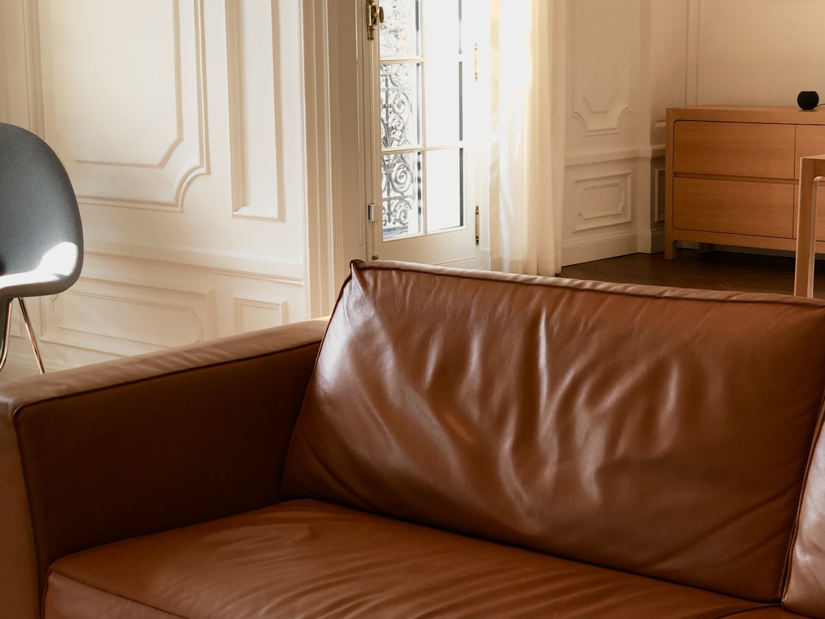 Brown leather sofa and a gray chair in a house with white walls and wooden furniture related to Leather Valances for Windows