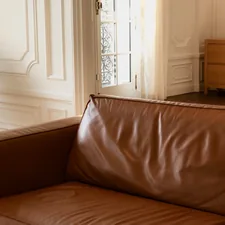 Brown leather sofa and a gray chair in a house with white walls and wooden furniture related to Leather Valances for Windows