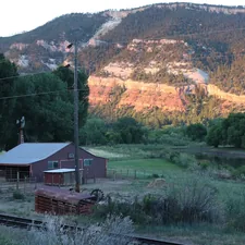 brown wooden house near green grass field and mountain during daytime related to Cozy Getaways in Durango, CO