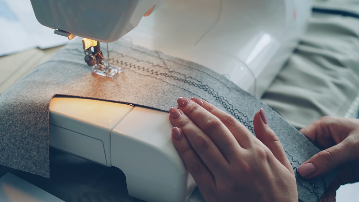 Close-up shot of working modern sewing machine, fabric and manicured female hand. Clothes manufacturing process concept. Light soft colours, beautiful stitches. related to Sewing Made Easy: Free Valance Patterns to Get You Started