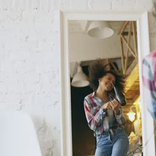 Curly funny mixed race girl dancing and singing with hair dryer in front of mirror at home related to Transform Your Space: Discovering Curtains at Bed Bath and Beyond