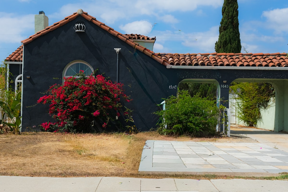 Dark house with red flowers and a carport. related to Elevate Your Home's Curb Appeal: Tips and Ideas for Your Pottery Barn Entryway