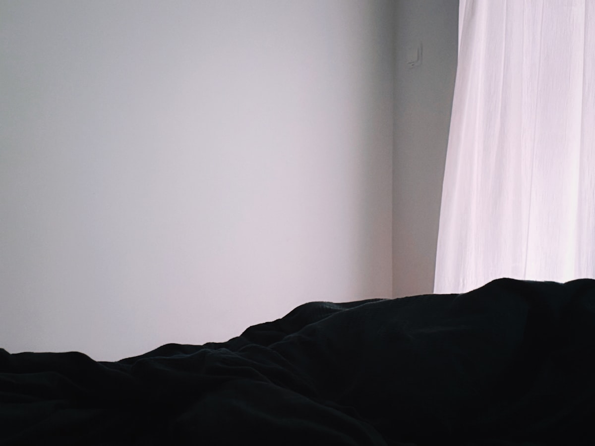 Dark rumpled fabric against a light wall and sheer curtain. related to Stylish Black and Pink Bedding Options
