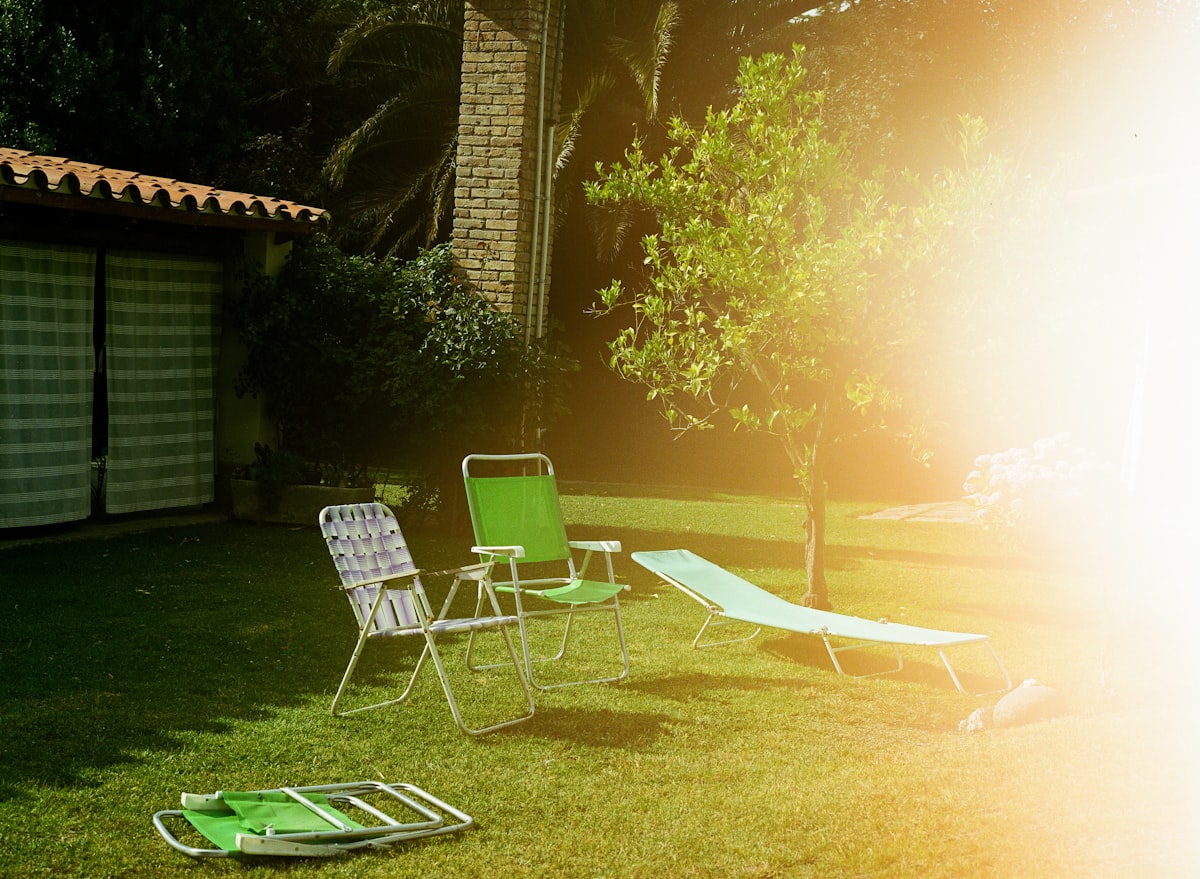 Empty garden chairs resting on green grass, flooded by intense sunlight. Shot on medium format film, embracing light leaks and imperfections as part of the analog process. related to Elevate Your Backyard Ambiance with a Chiminea Stand Iron