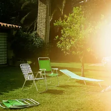 Empty garden chairs resting on green grass, flooded by intense sunlight. Shot on medium format film, embracing light leaks and imperfections as part of the analog process. related to Elevate Your Backyard Ambiance with a Chiminea Stand Iron